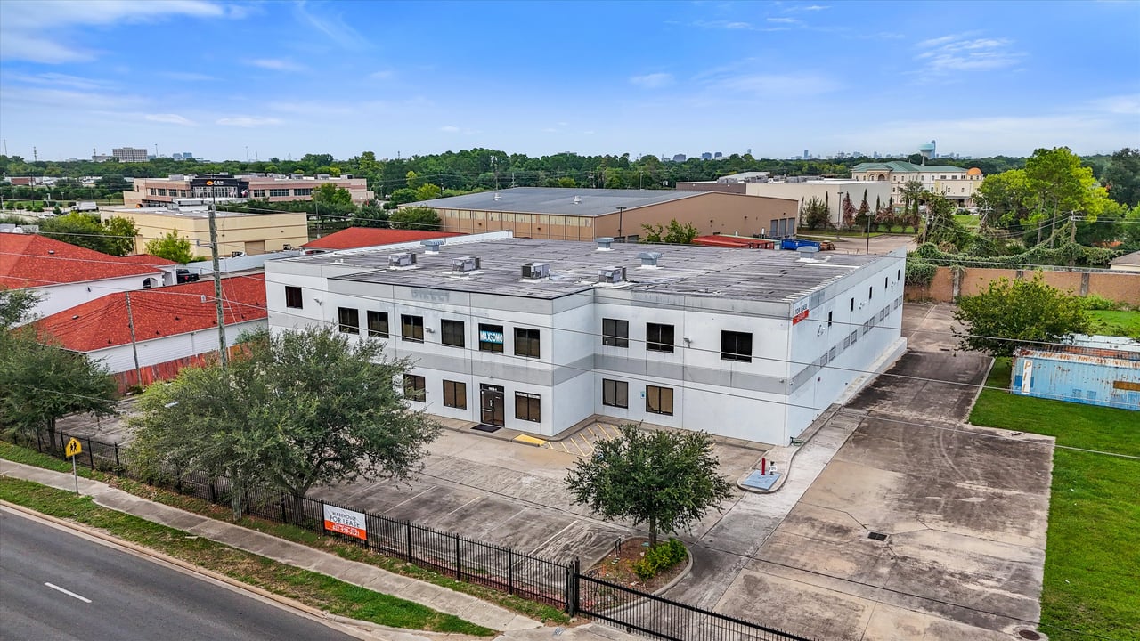 Two-story white commercial building with a flat roof and paved parking lot, viewed from above.