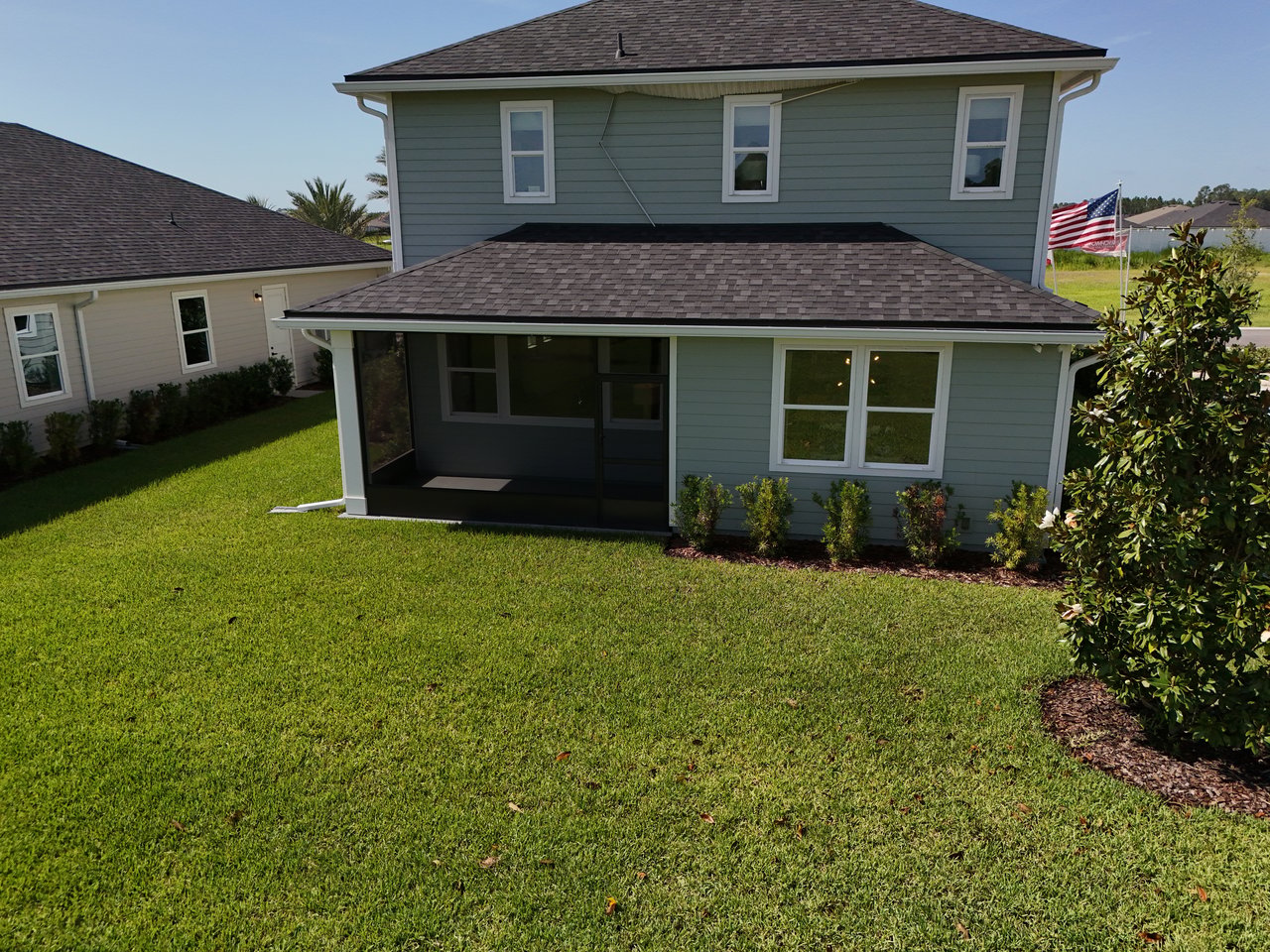 Rear of a two-story blue-gray home with a covered porch and broad green lawn.
