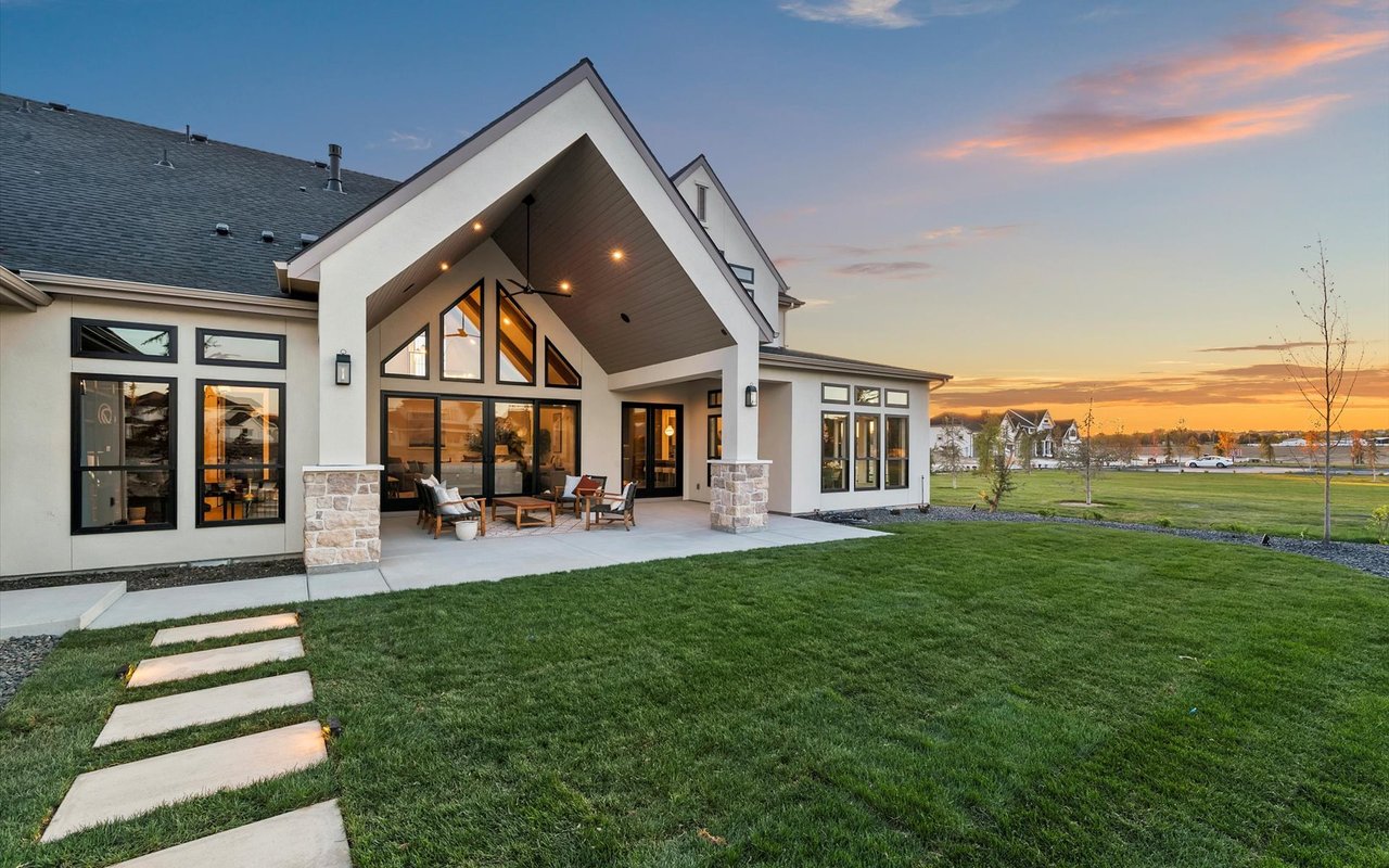 Back exterior of the home showing the green lawn, stone pavers, and the greenspace to the west of the property