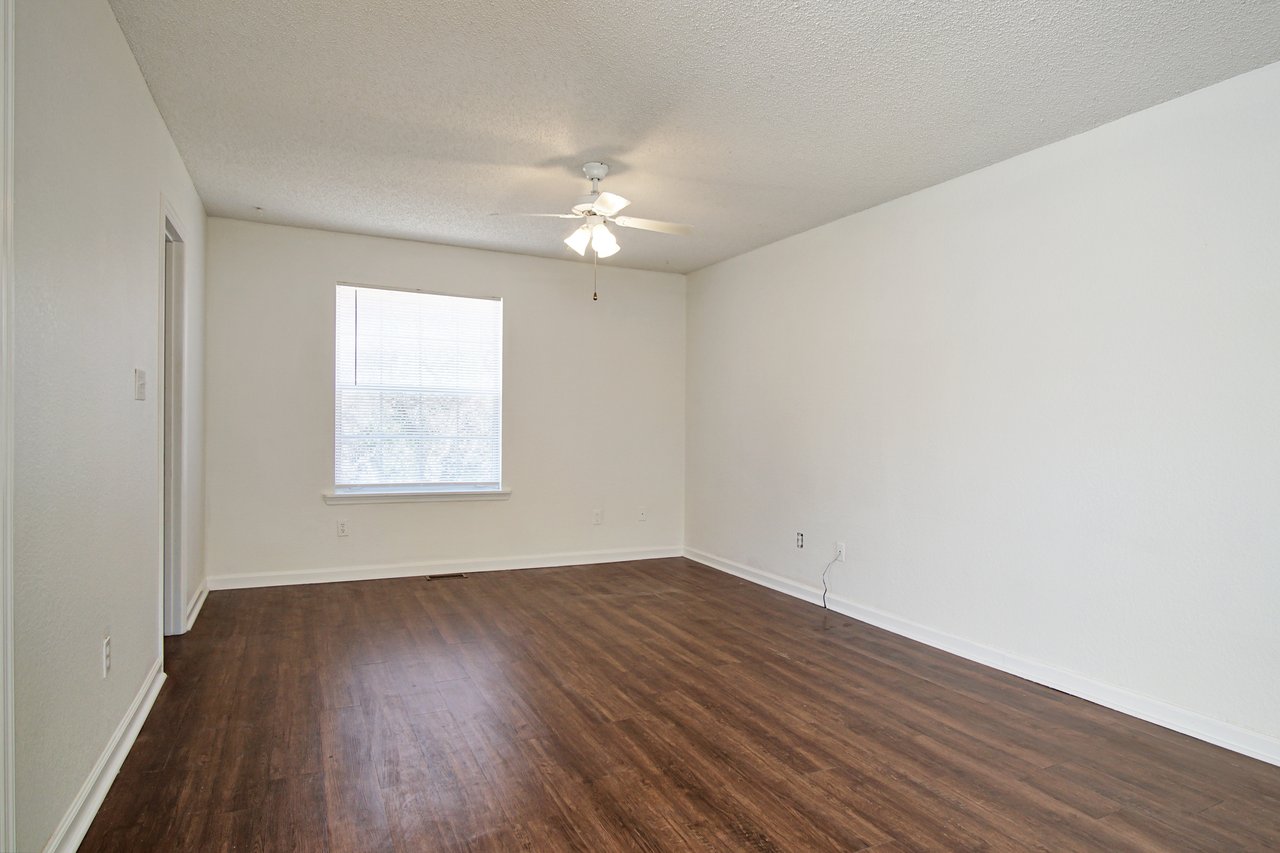 An empty room featuring hardwood floors and a ceiling fan, creating a spacious and airy atmosphere.