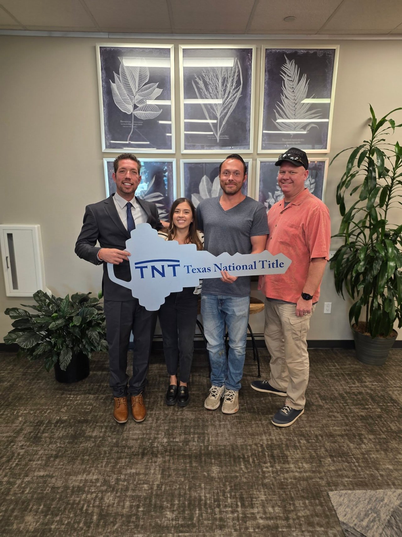 Four adults pose with a Texas National Title sign inside an office.