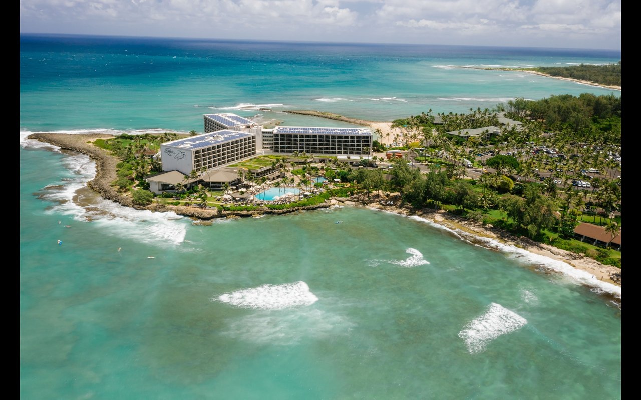 Coastal resort on Kahuku’s shore, surrounded by turquoise water and palm trees.