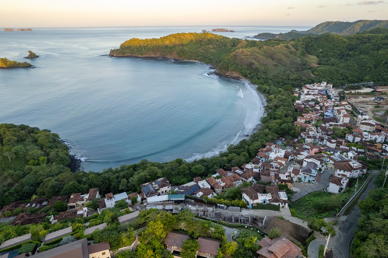 A coastal town wraps around a bay beneath forested hills, with small islands offshore.