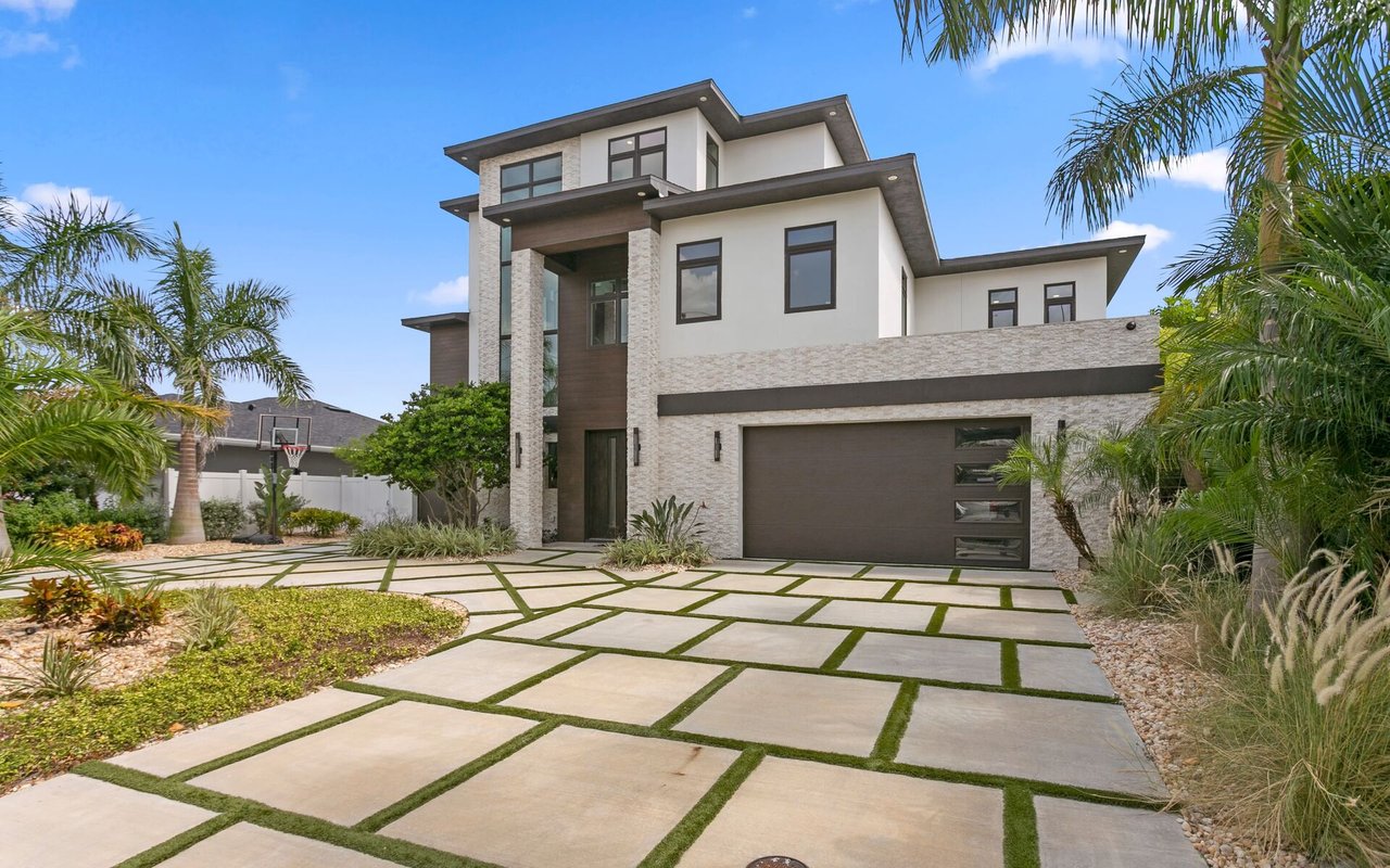 Modern two-story home with a stone-and-white facade, dark garage, and geometric grass-jointed driveway.
