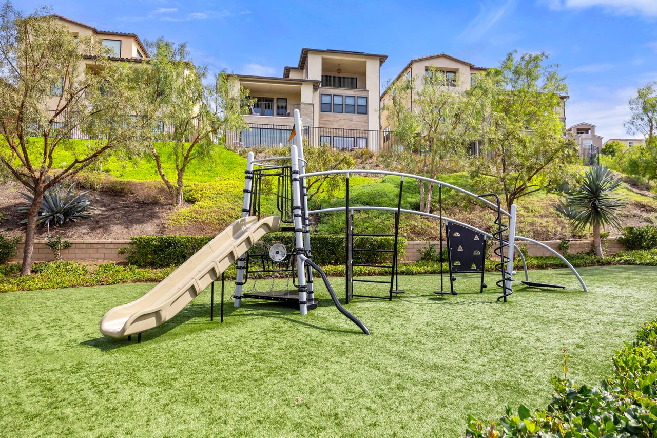 Neighborhood playground with a slide and climbing structure in front of landscaped homes.