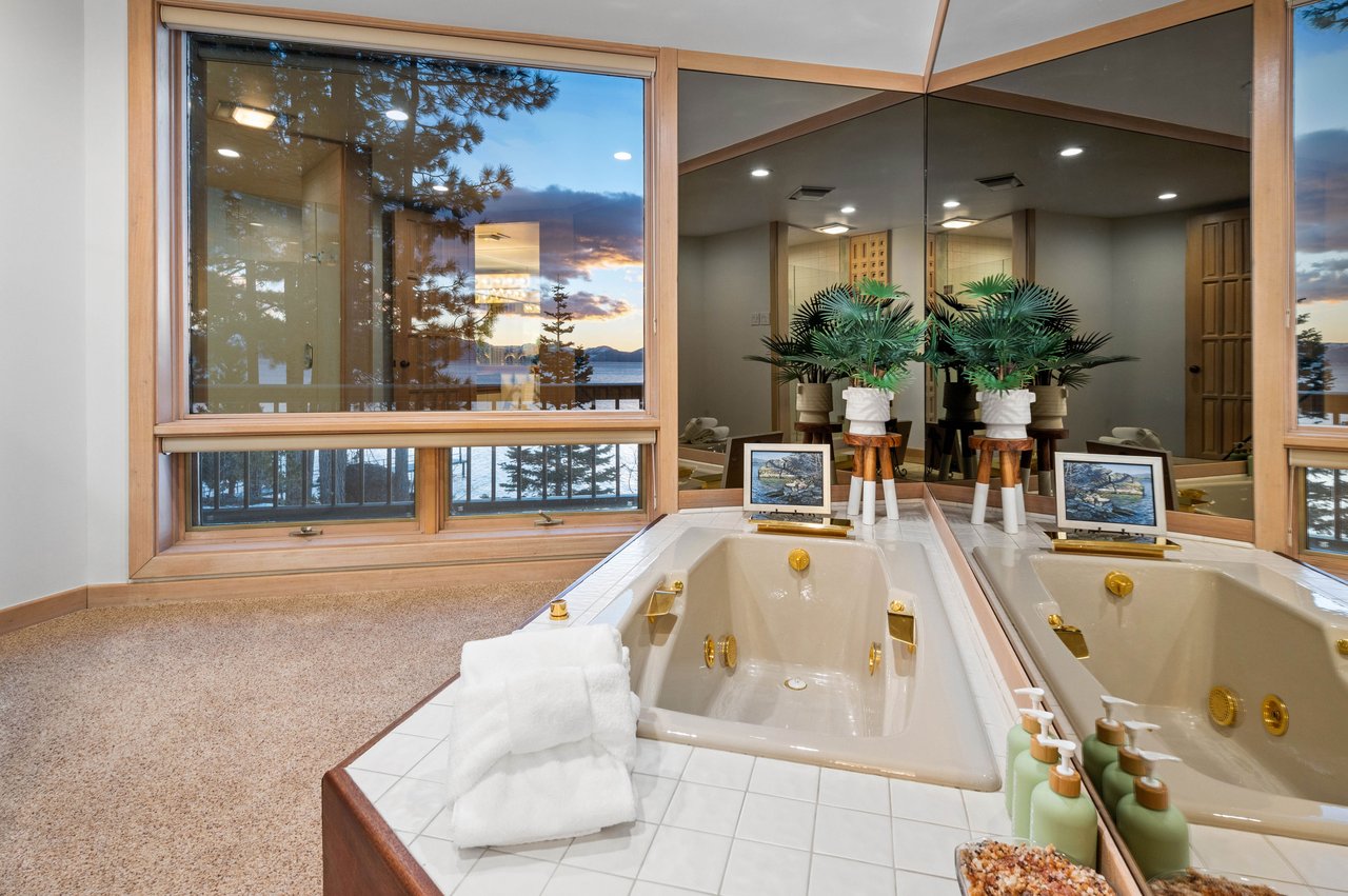 Bathroom with a jetted tub, mirrored walls, and sunset lake views through large windows.