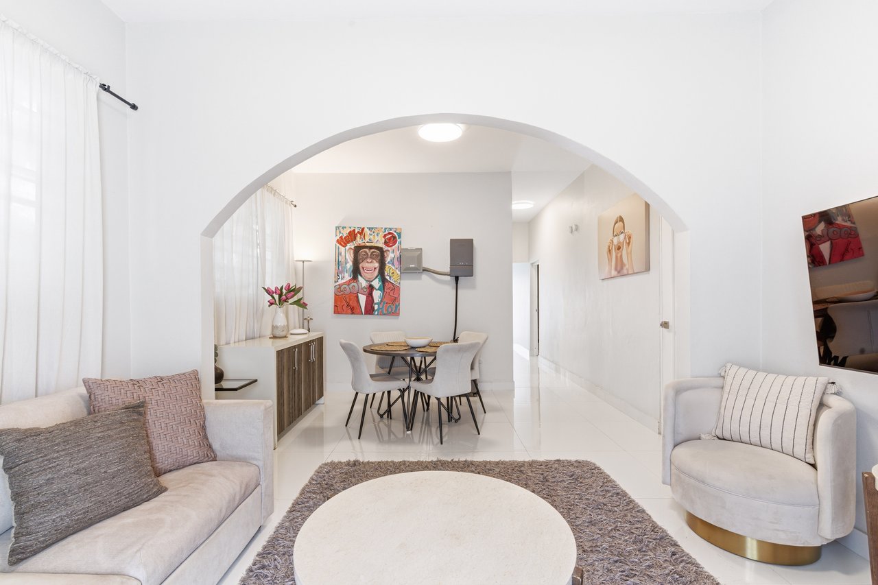 Furnished living room with an arched opening to a dining area and colorful wall art.