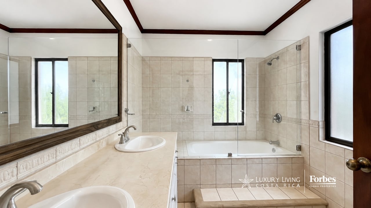 Tiled bathroom with a bathtub, glass shower screen, and long mirrored vanity.