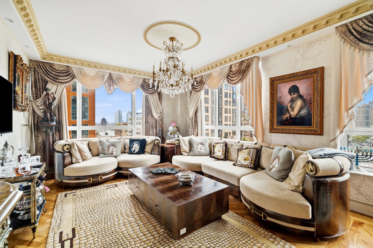 Ornate Manhattan living room with curved cream sofas, chandelier, and city views through large windows.