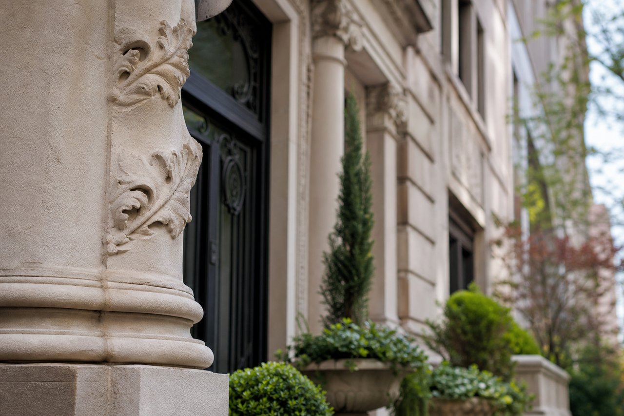 Residential building entrance with carved limestone columns, a dark door, and landscaped shrubs.