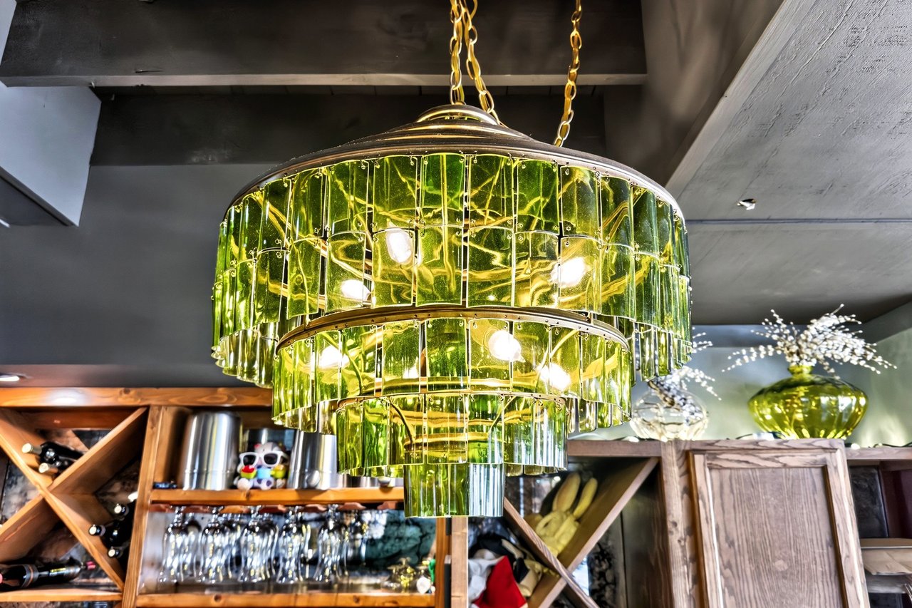 Green glass chandelier above a restaurant bar with wooden wine shelving.