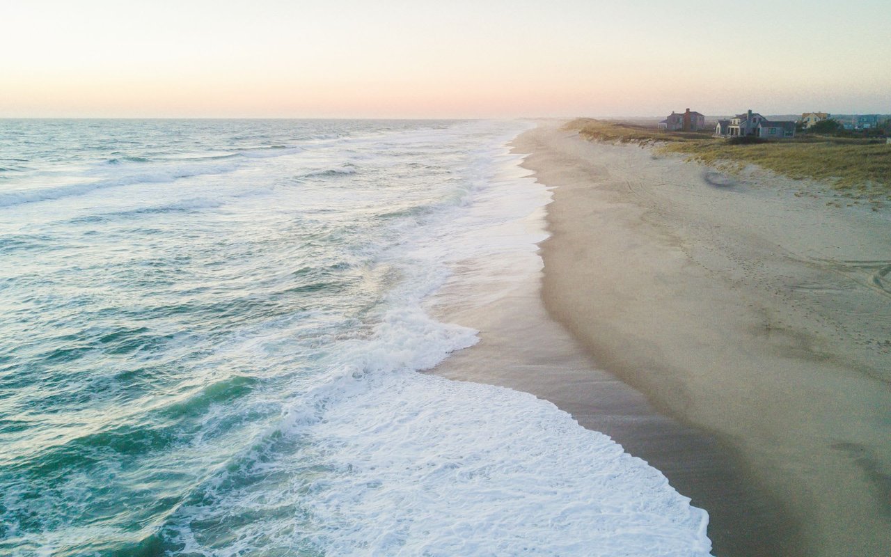 Ocean waves crashing on the beach in Pocomo with houses in the distance.