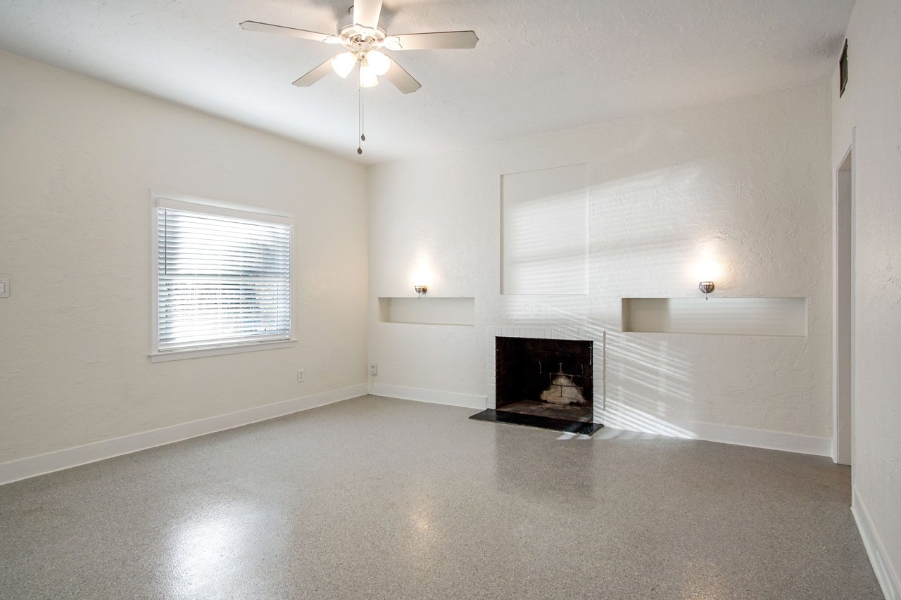An interior shot of a living room with a fireplace, large windows, and tiled flooring. The room is spacious and well-lit.