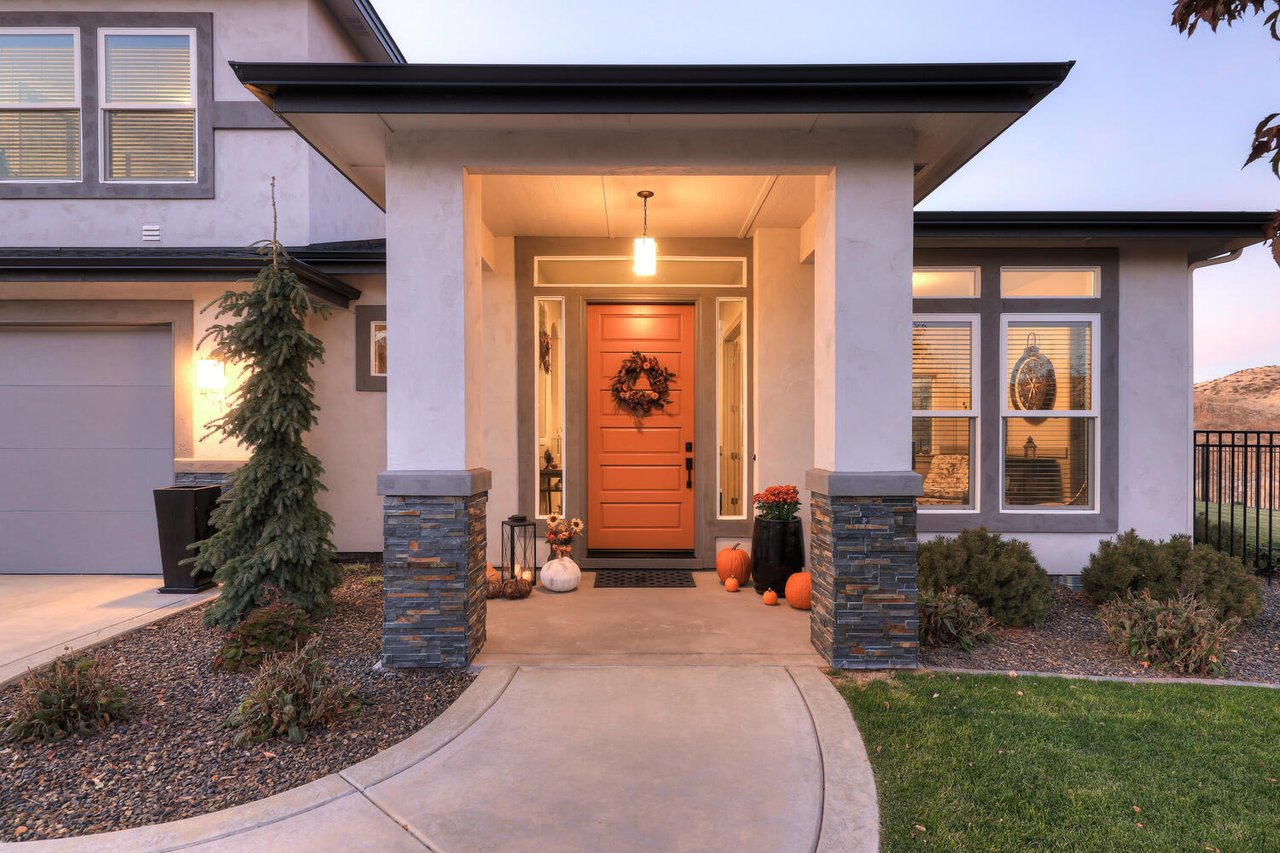  A modern stucco house with a light gray exterior and a striking orange front door adorned with a wreath.
