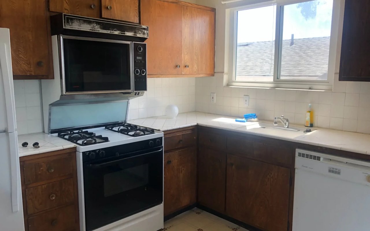 A Before photo of a small kitchen in Philadelphia with white cabinets, a stove, microwave, dishwasher, and sink.