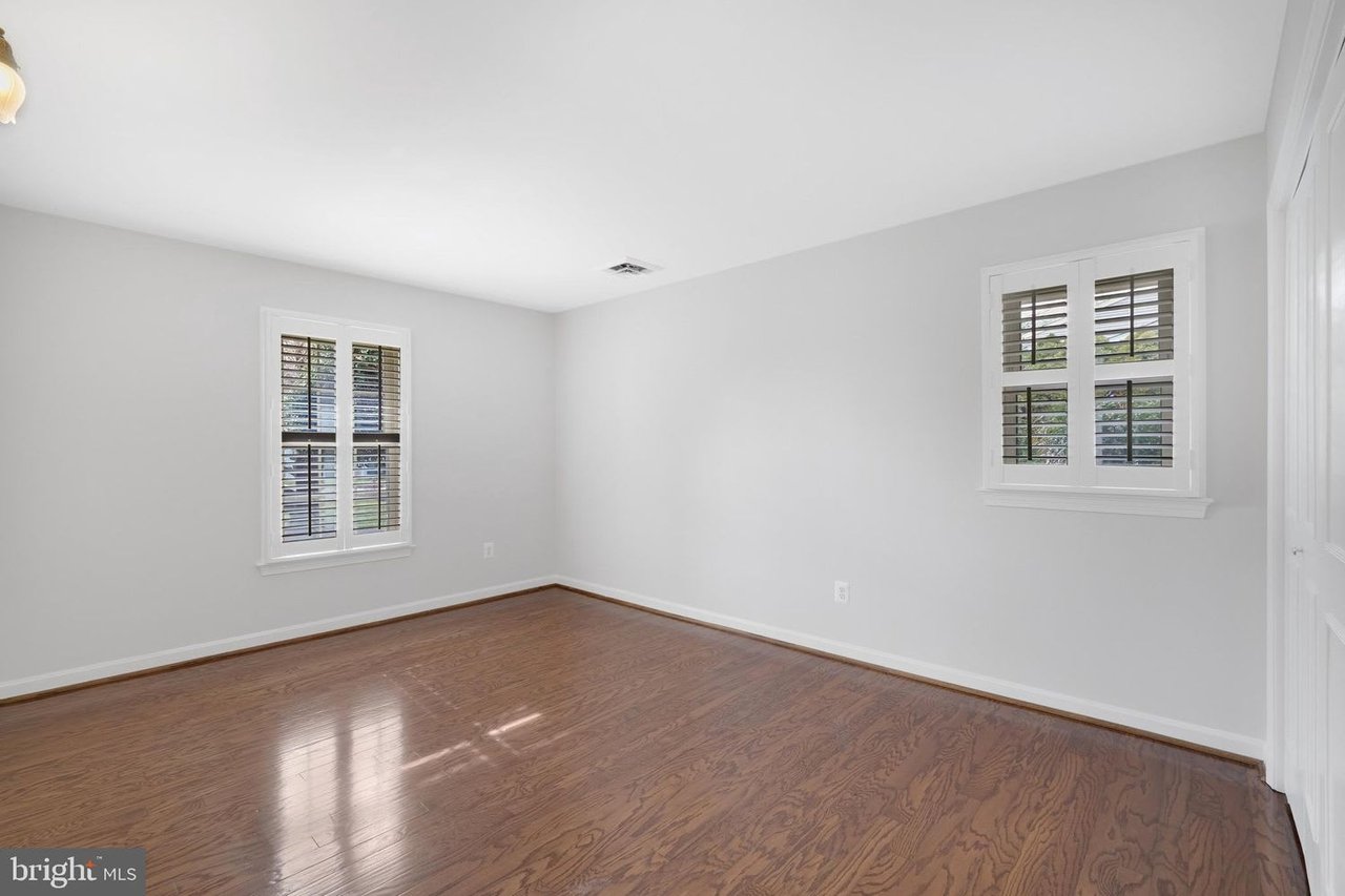 Empty room with hardwood floors and two shuttered windows.