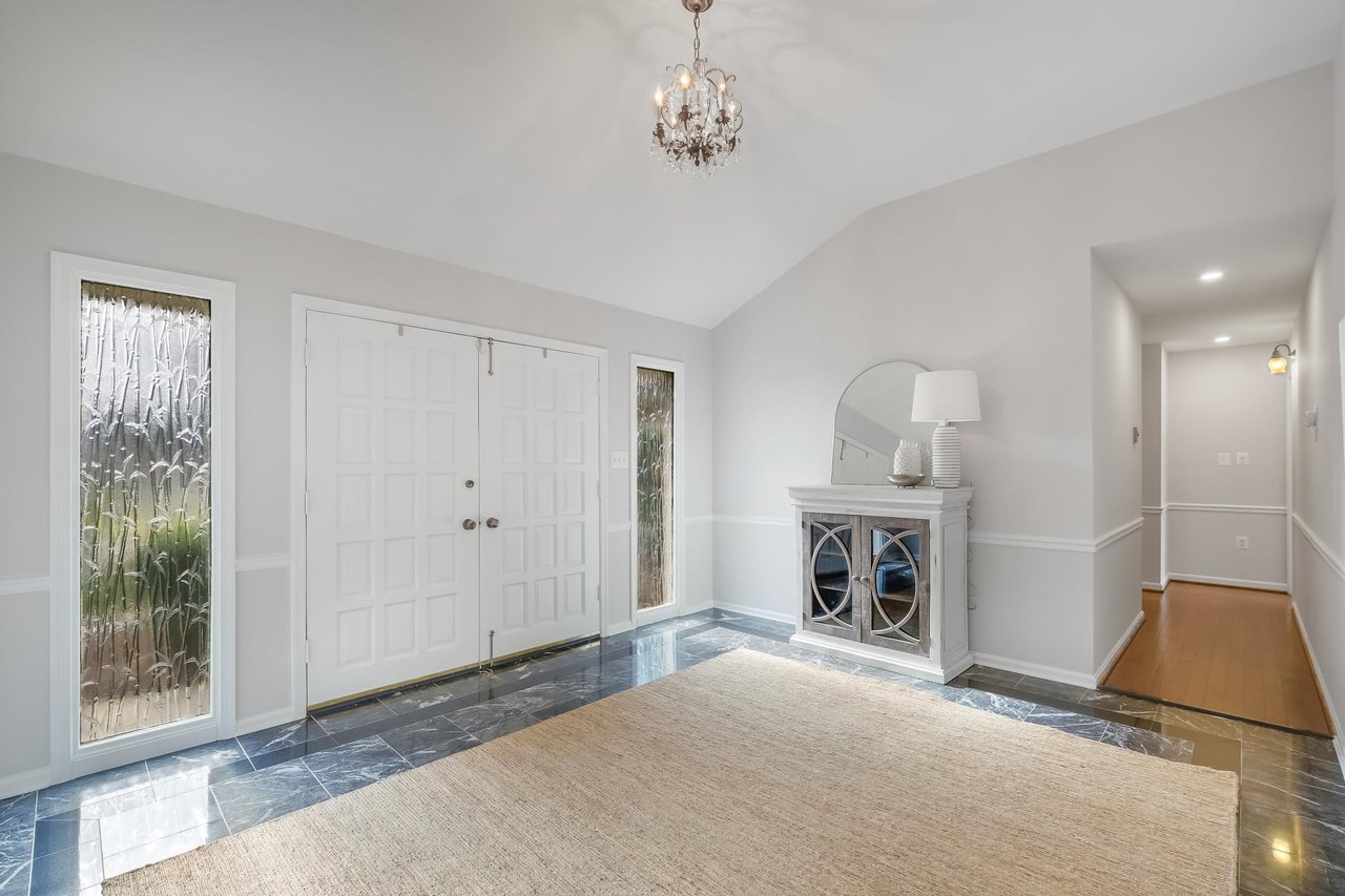 Entry foyer with white double doors, decorative glass sidelights, marble tile, and a chandelier.