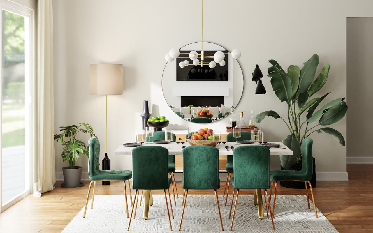 Chic dining area with green velvet chairs, marble table, large circular mirror, and lush indoor plants.