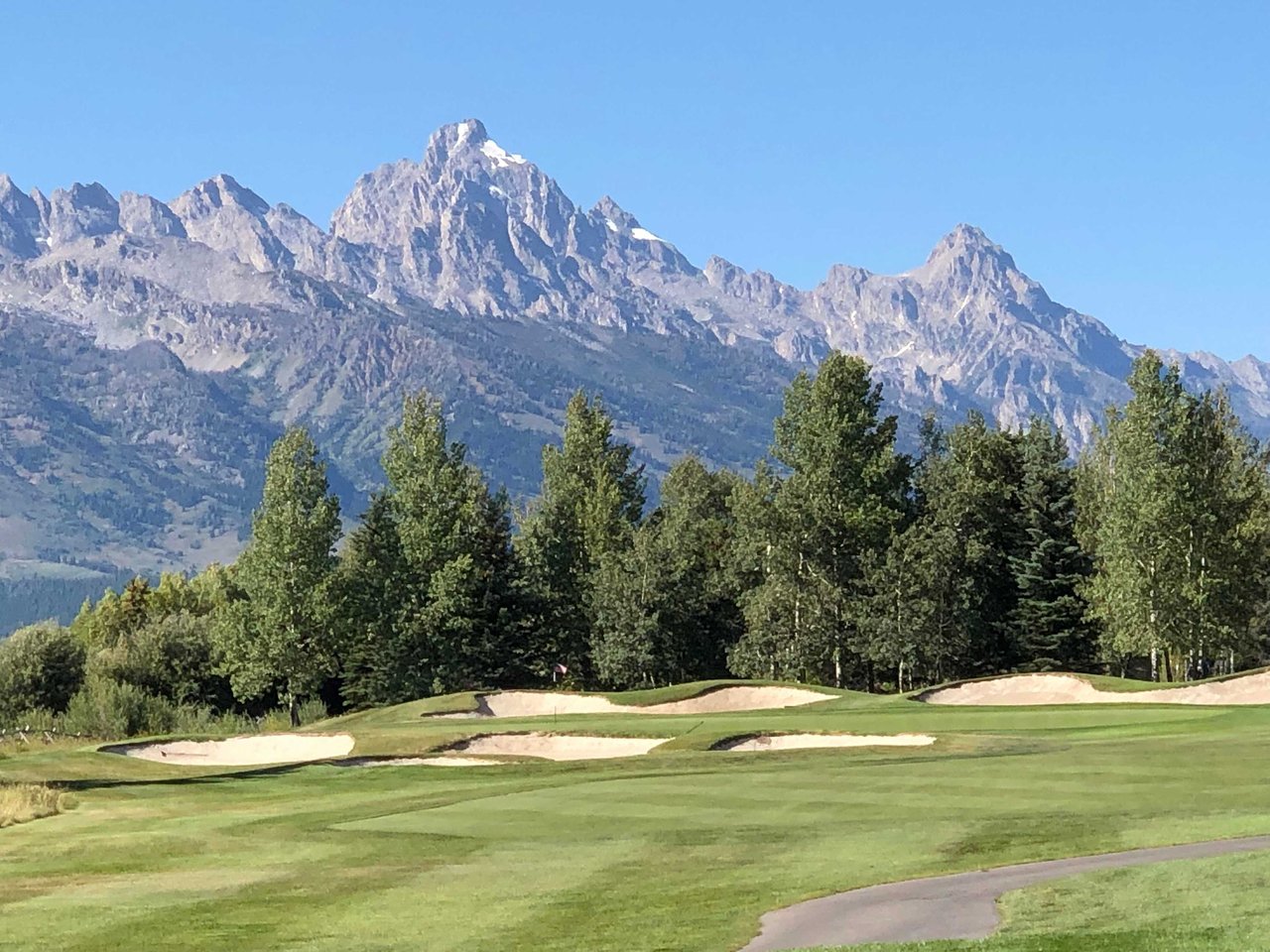 Aerial view of a stunning golf course in Jackson Hole with mountain views, lush greens, and luxury homes nearby, showcasing the perfect golf and outdoor lifestyle in Wyoming.