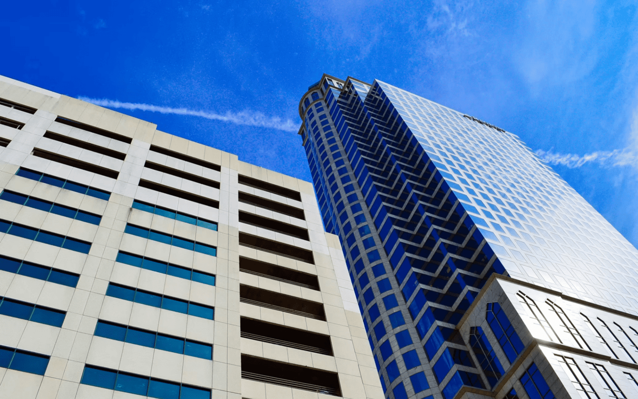  A low-angle view of two tall buildings against a bright blue sky with wispy white clouds.