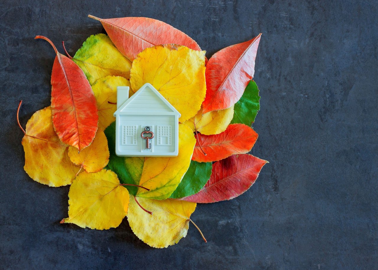 White model house and key surrounded by colorful autumn leaves.