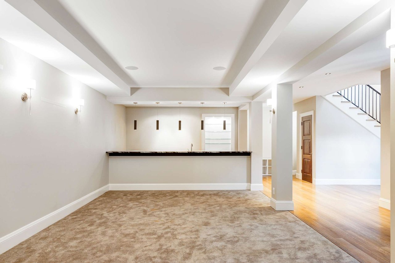  inished basement with wet bar, pendant lights, carpeted floor, and hardwood hallway leading to stairs