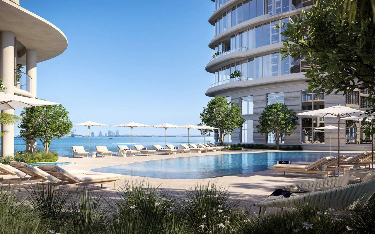 Pool terrace with lounge chairs and umbrellas beside a waterfront high-rise.