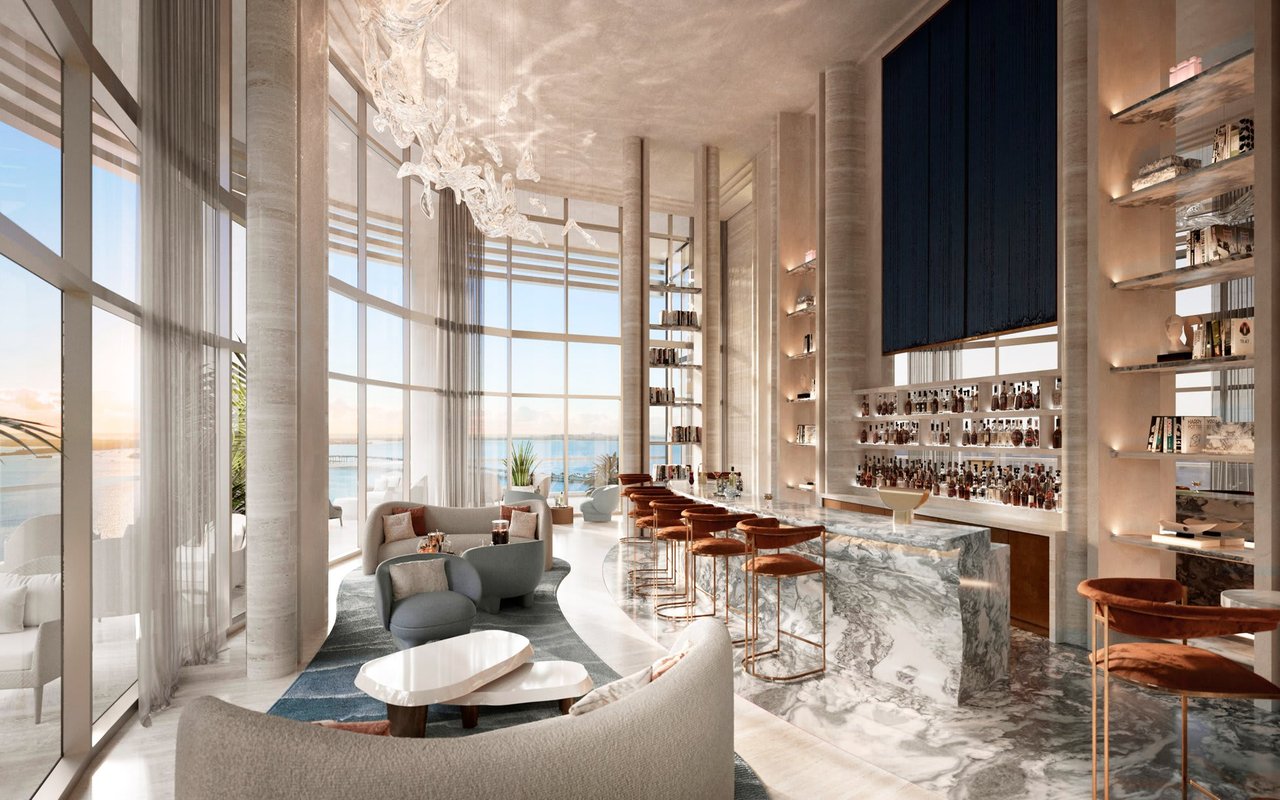 Luxury lounge and bar with a marble counter, curved seating, and floor-to-ceiling water views.