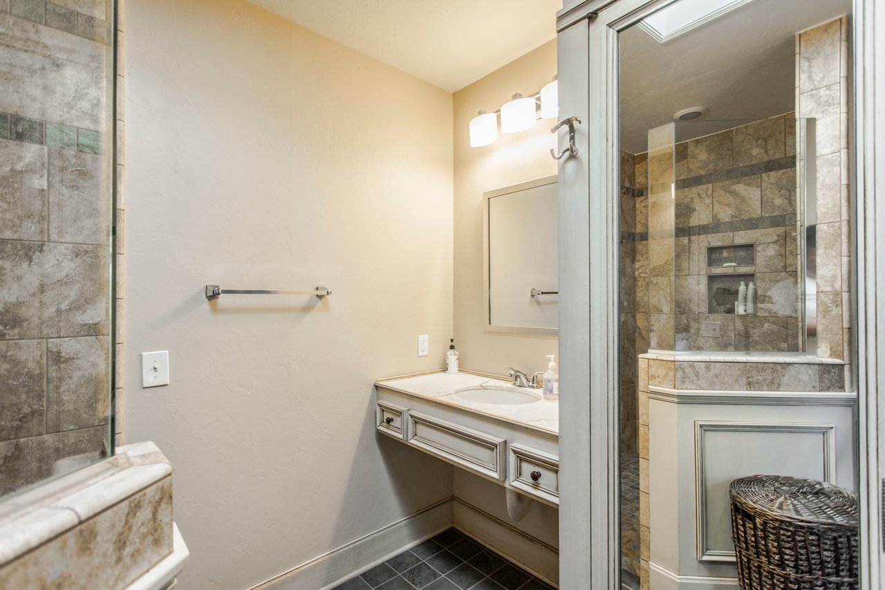 Bathroom with a white vanity and glass shower tiled in mottled stone-look tile.