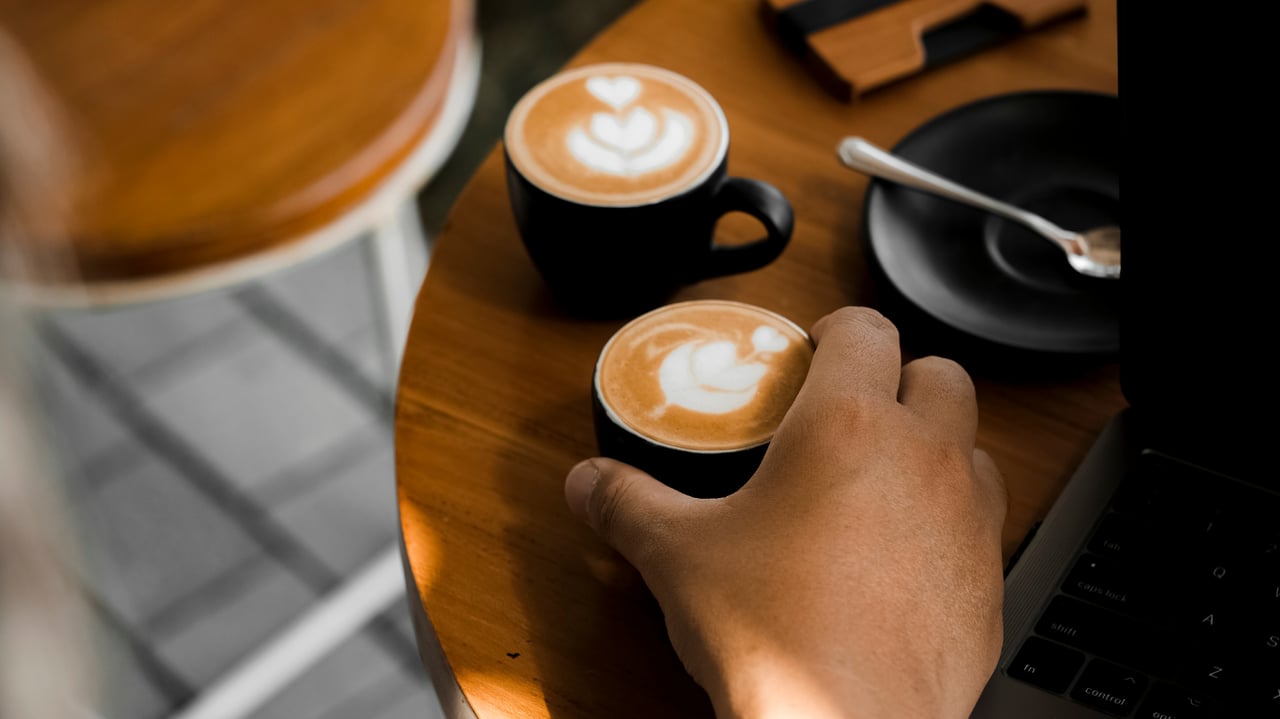 Hand reaching for a latte with heart-shaped foam art at a café table