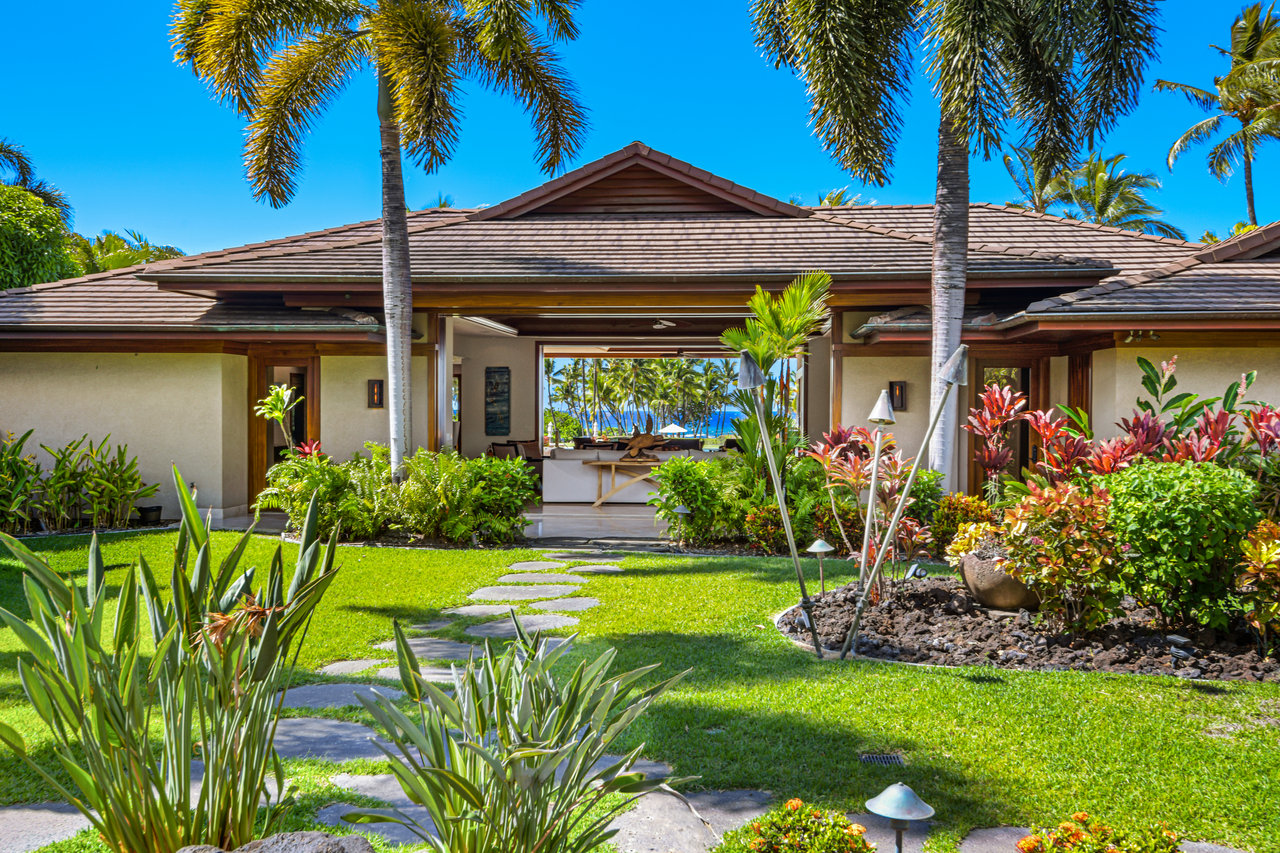 Tropical home framed by palms and lush gardens, with an ocean view through the open entrance.