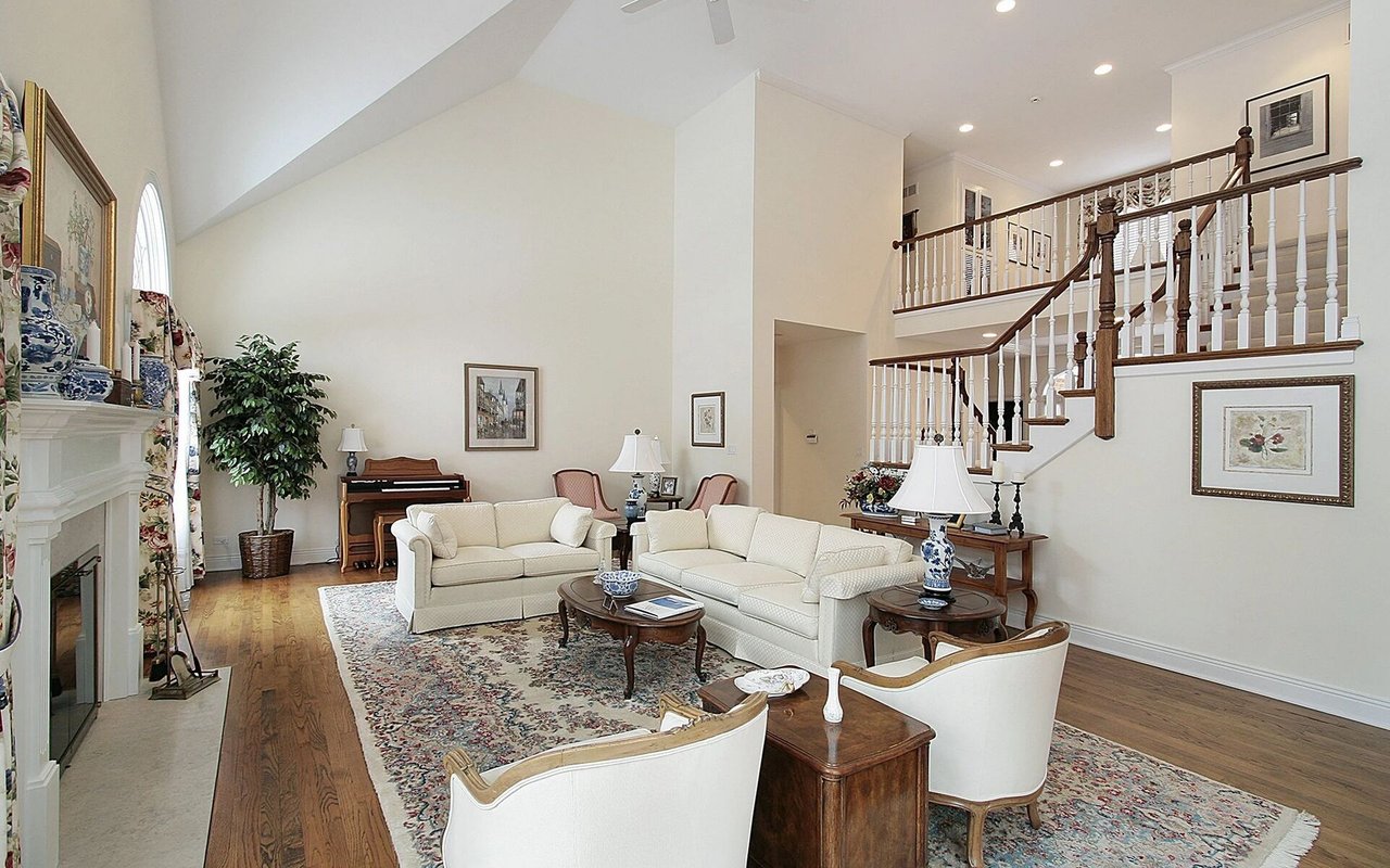 Living room with vaulted ceilings, a fireplace, cream seating, and a prominent staircase.