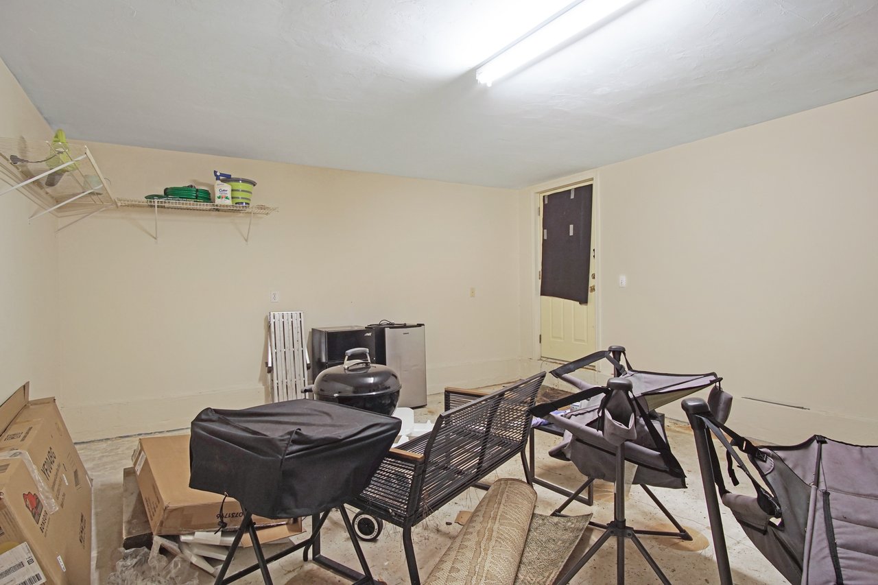 Basement storage area at 529 Collinsford Road, Tallahassee, Florida, featuring beige walls, a fluorescent ceiling light, and a door leading outside. A wire storage shelf is mounted on the wall.