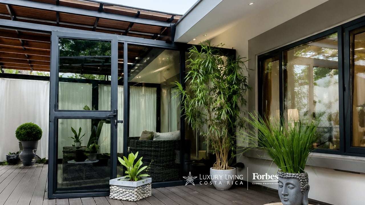 Covered patio with glass doors, wicker seating, timber decking, and potted plants.
