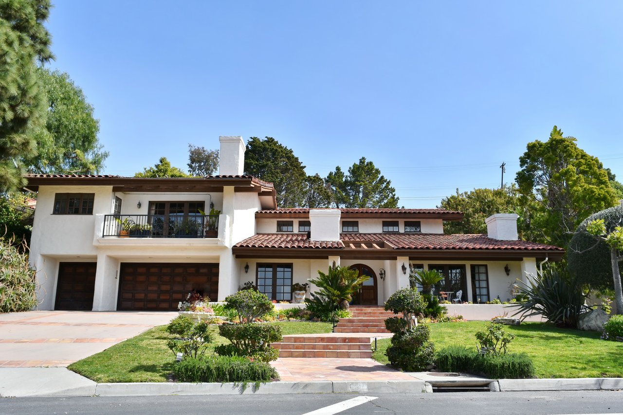 Two-story stucco home with a red tile roof, balcony, double garage, and landscaped front lawn.