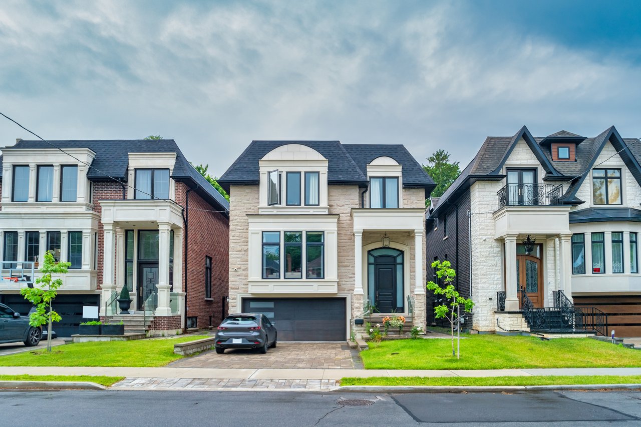 Stone-fronted home with a dark garage, lawn, and neighboring houses along the street.