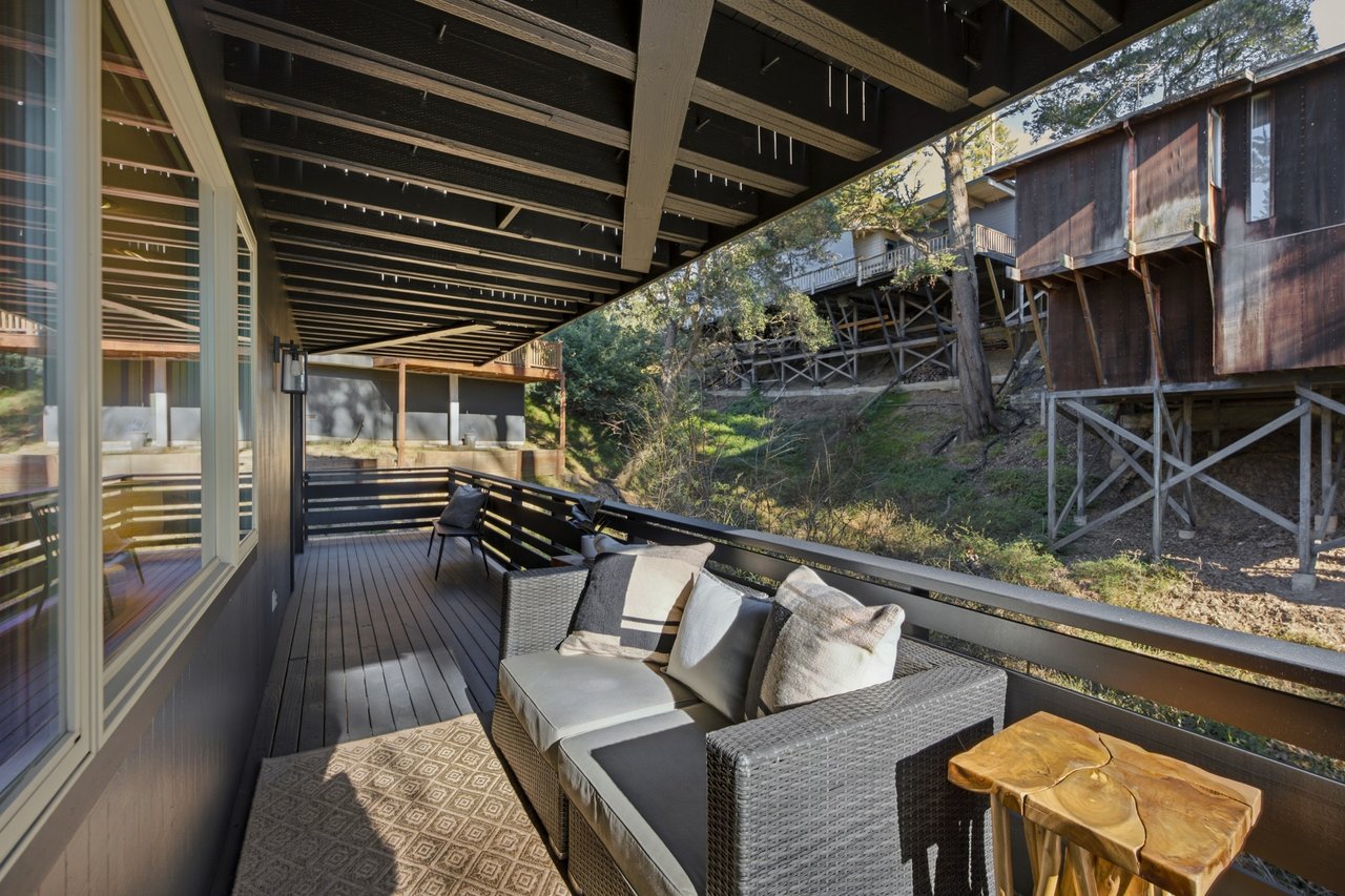 Covered deck with wicker seating and a view of the wooded hillside.