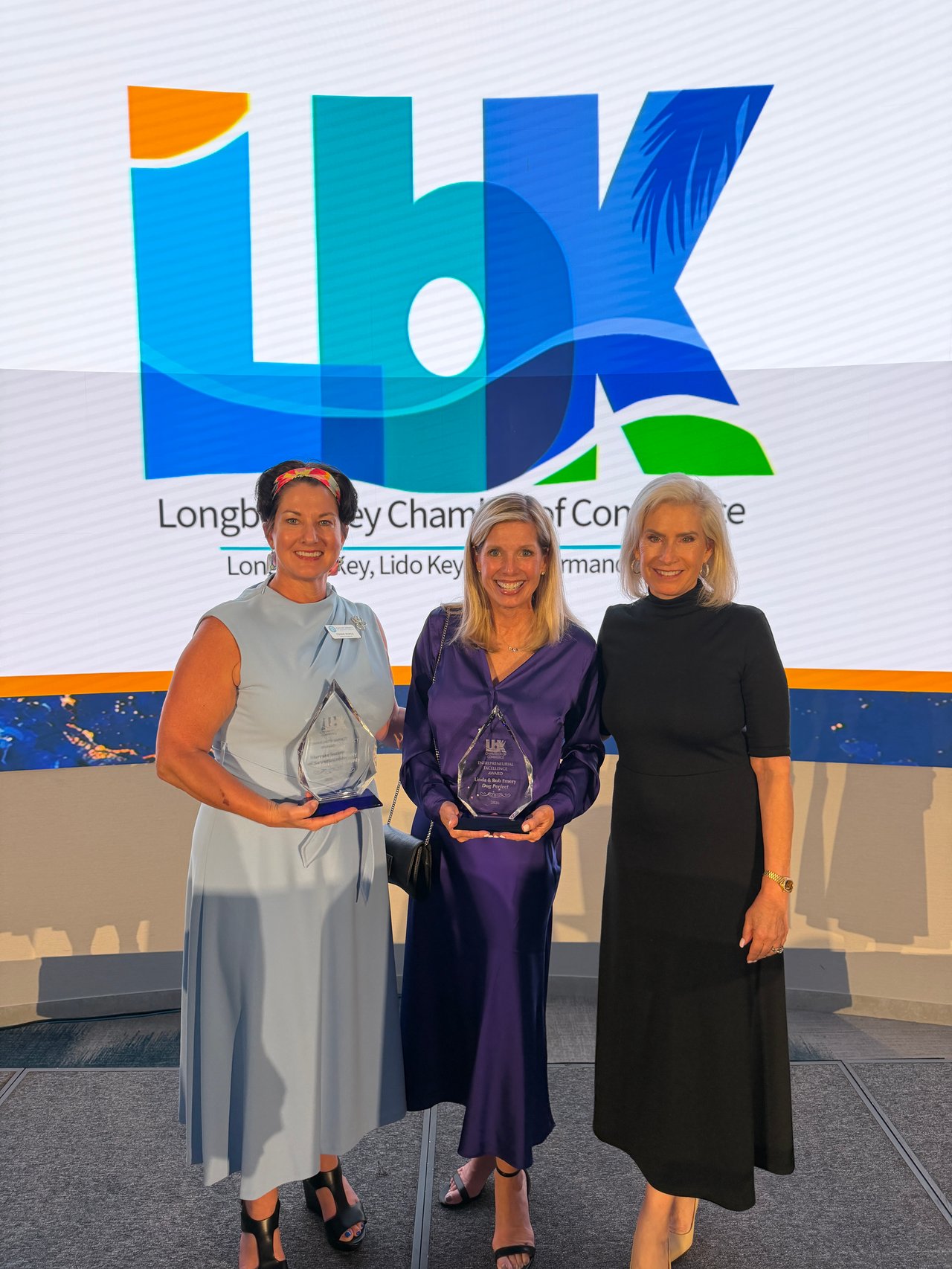 Three women pose with awards in front of the Longboat Key Chamber of Commerce backdrop.