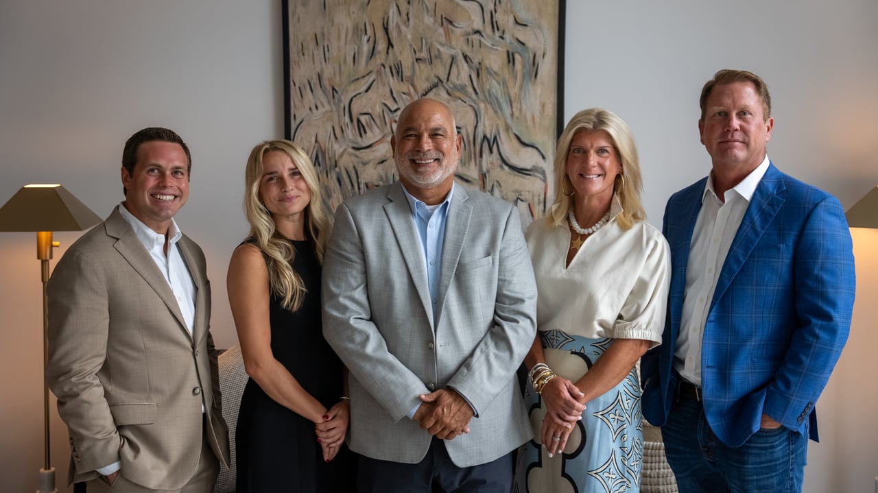 Five real estate team members pose in business attire in front of an abstract painting.