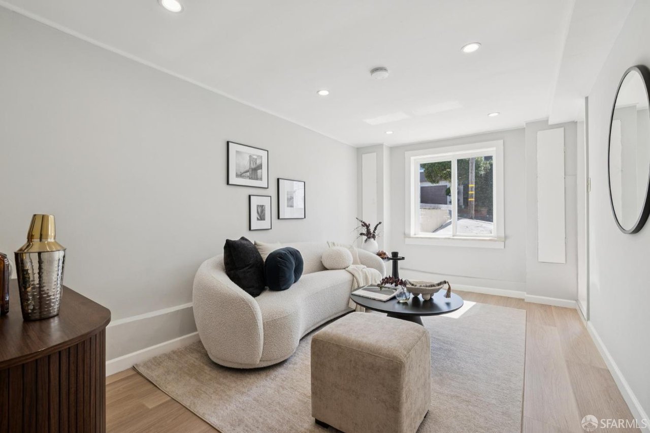 Furnished living room with a curved white sofa, round coffee table, and large window.