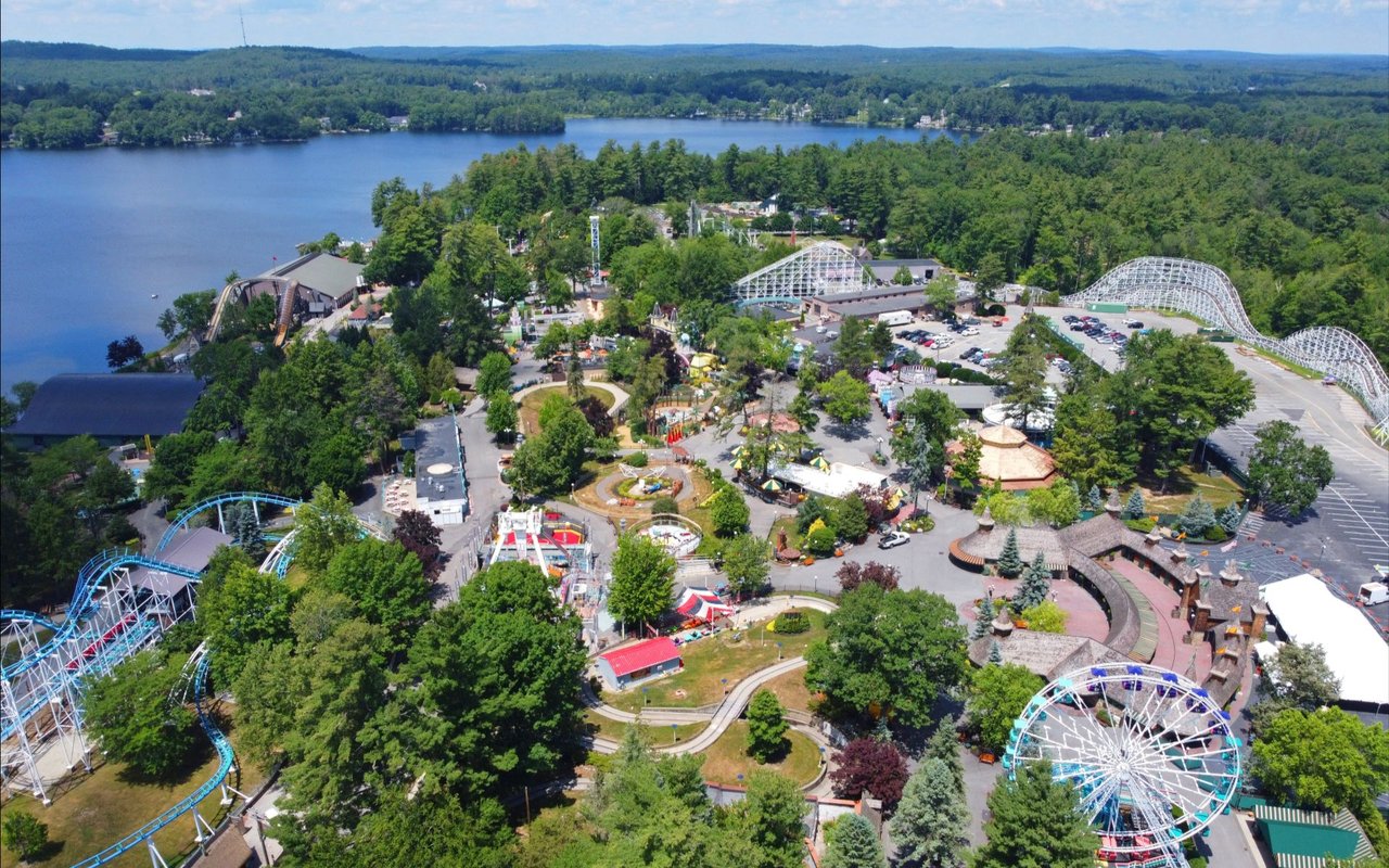 Aerial view of Salem amusement park beside a lake, with roller coasters and wooded shoreline.