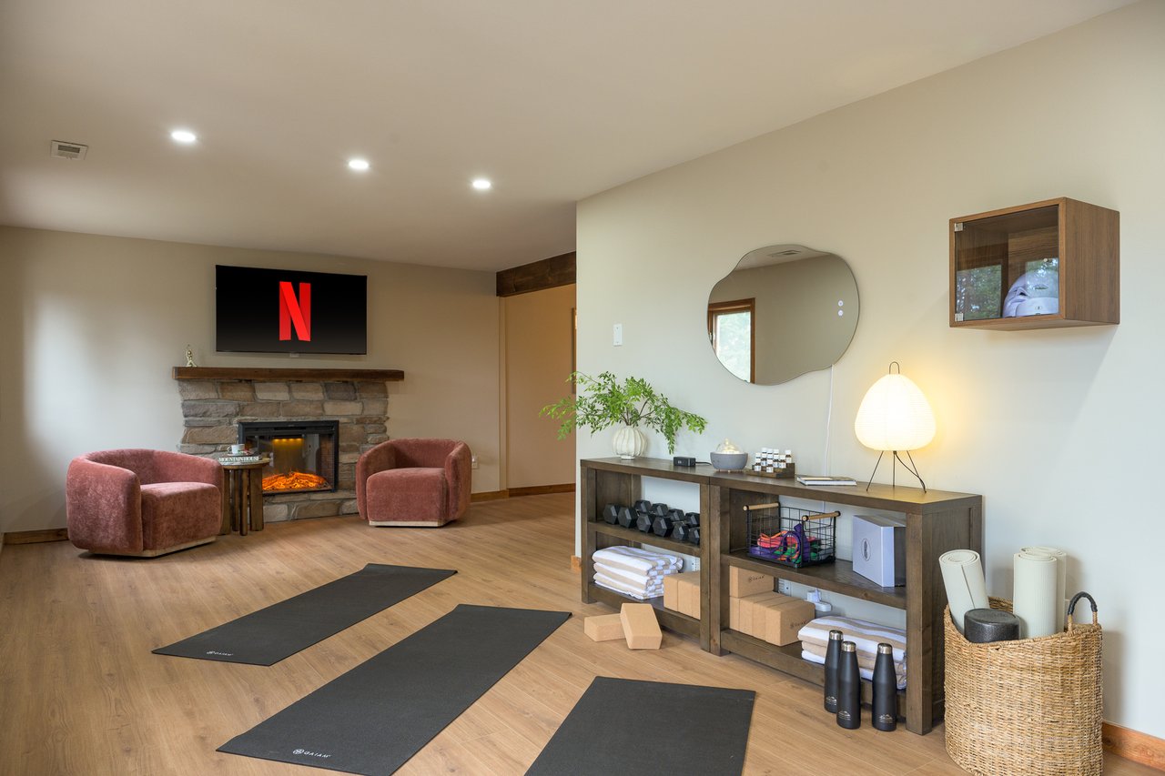 Furnished home fitness room with exercise mats, a stone fireplace, and dusty rose armchairs.
