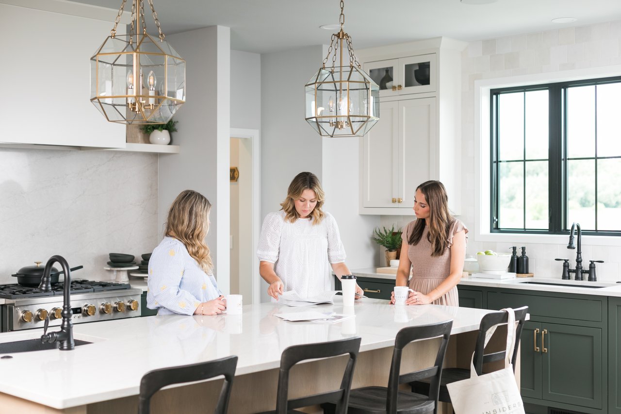 Three people gathered around a kitchen island reviewing documents together while working through the sale of a family home.