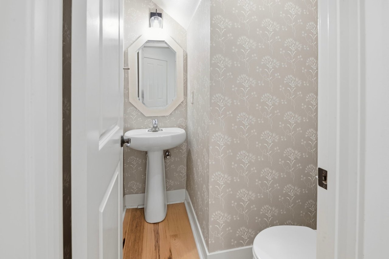 Powder room with pedestal sink, hexagonal mirror, decorative wallpaper accent wall, and sconce lighting