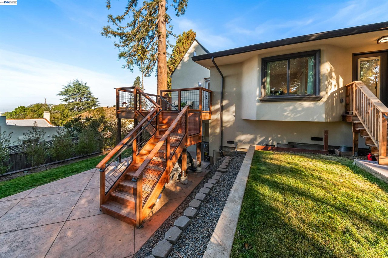 Home’s rear exterior with a raised wood deck, broad stairs, and a small lawn.