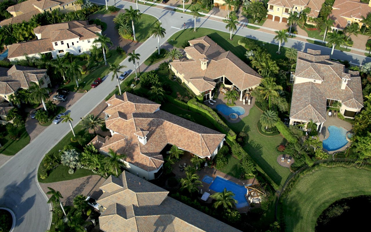 Aerial view of homes with tile roofs, pools, palm trees, and curving streets.