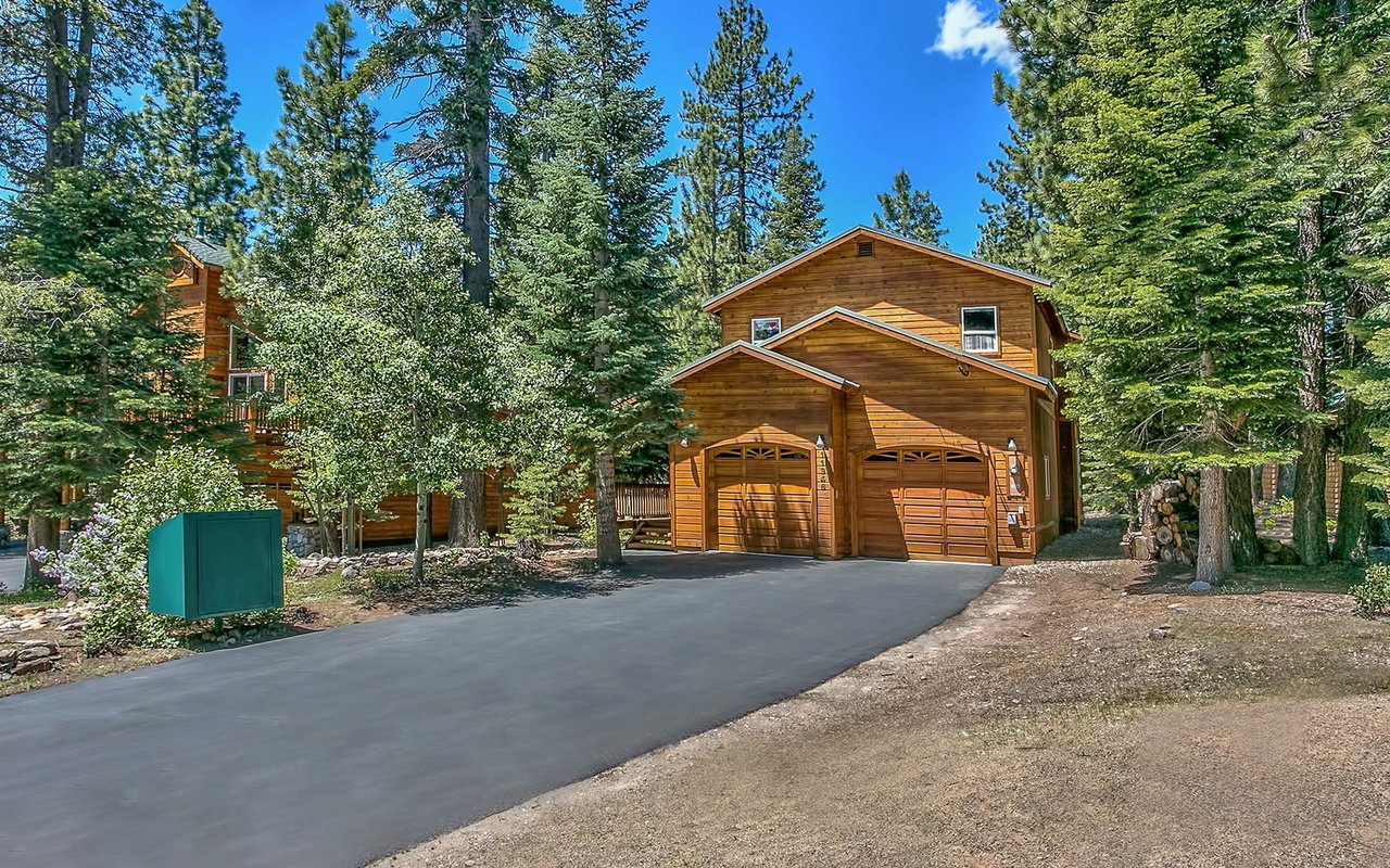 Wood-sided home with a two-car garage and paved driveway among tall pine trees.