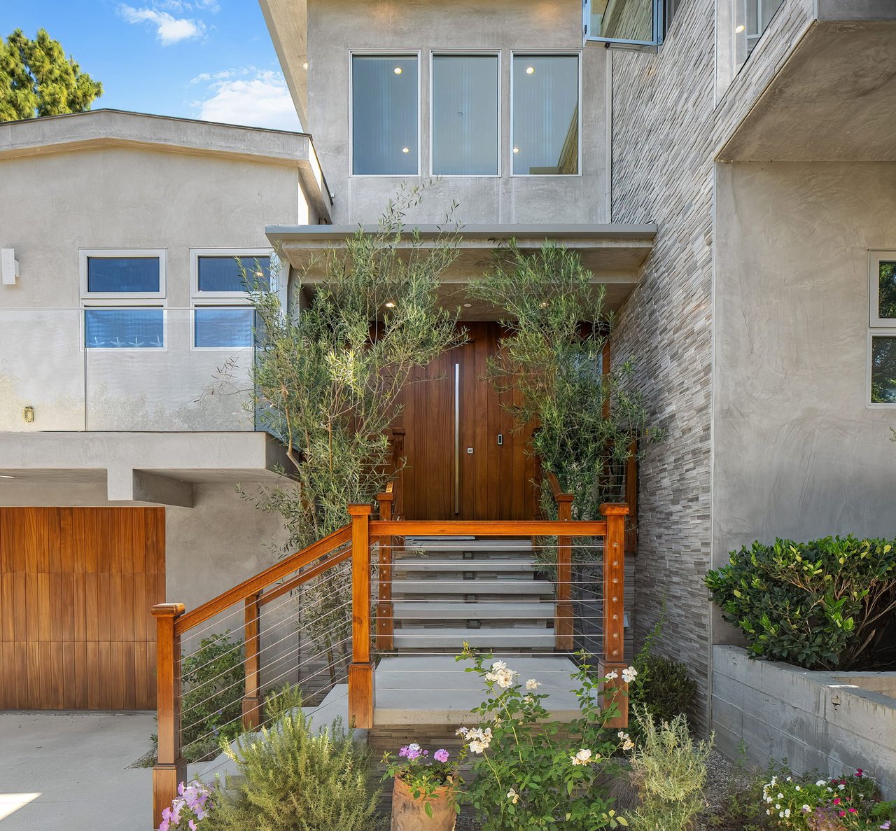 Modern home entrance with broad steps, a wooden front door, and landscaped planting beds.