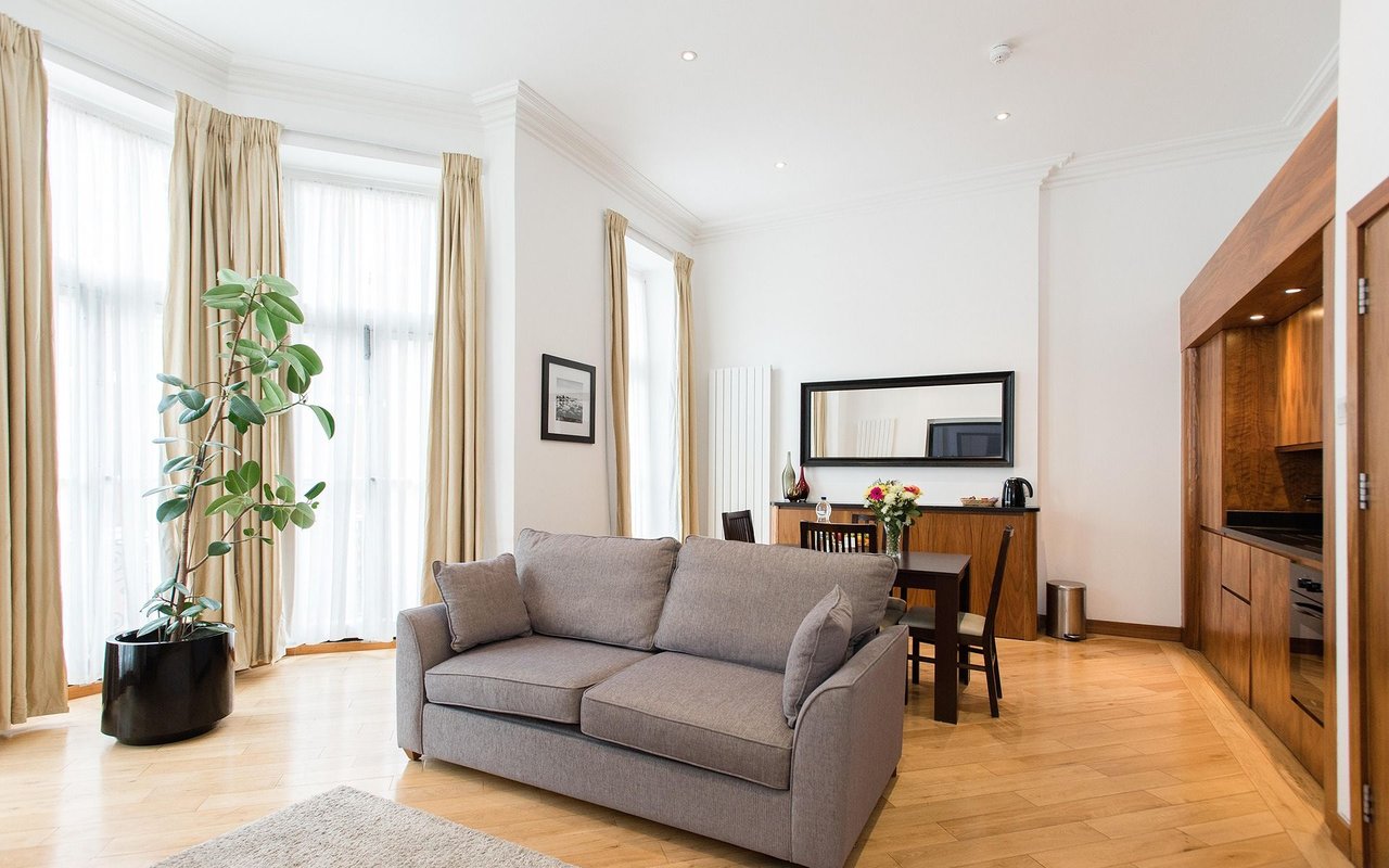 Living room with a gray sofa, tall curtained windows, parquet floors, and built-in wood cabinetry.