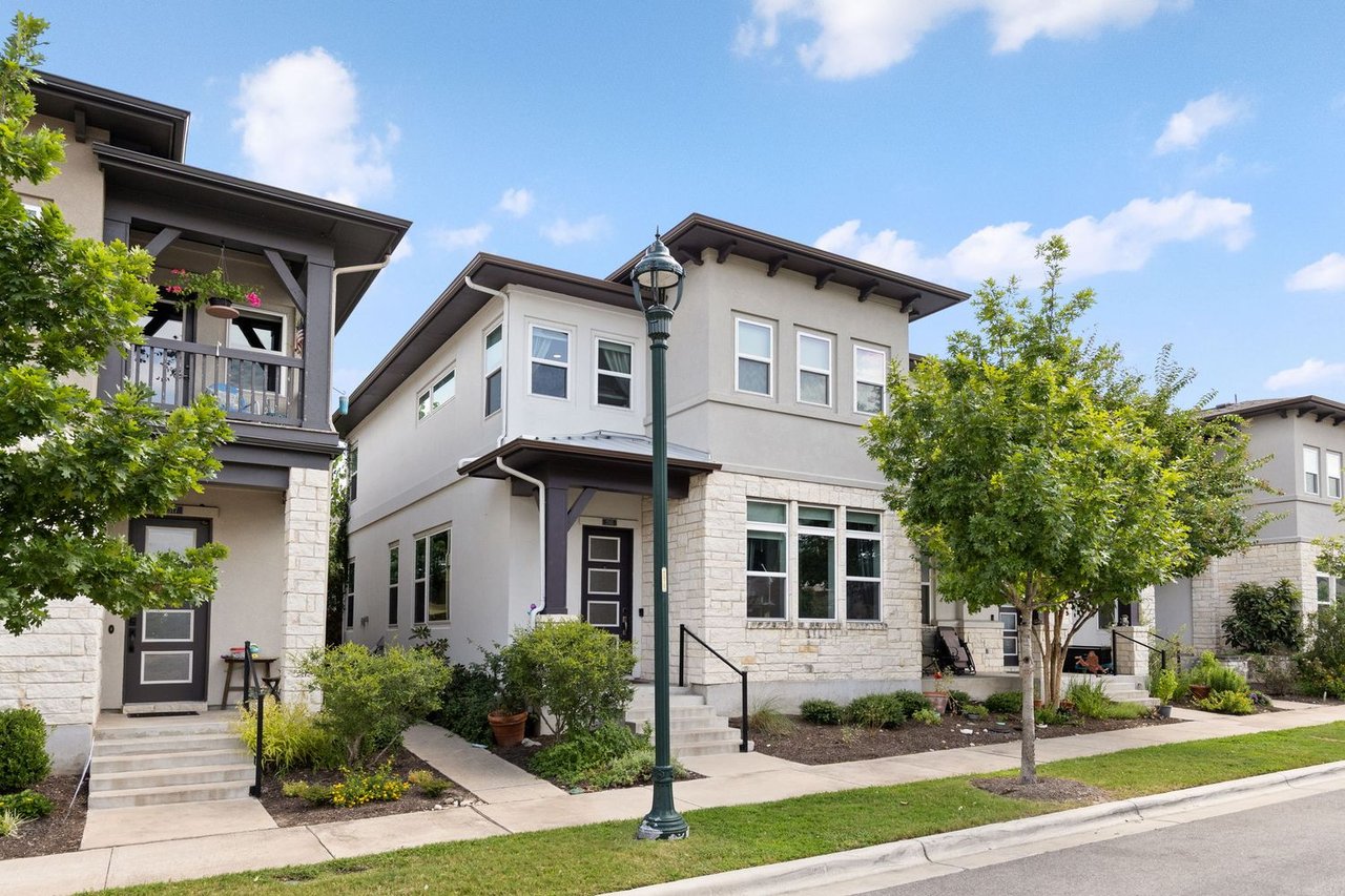 Two-story stucco home with stone facing, dark trim, and landscaped front steps.